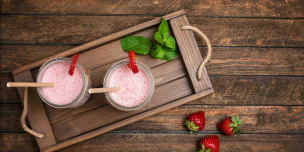 Fresh strawberry smoothie or milkshake and berries on wooden tray on wooden background. Top view. Healthy eating concept